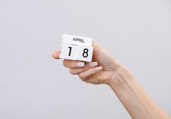 Block calendar with date april 18 in female hand on gray background