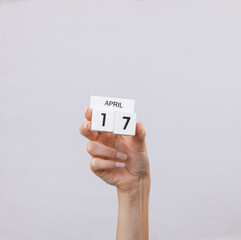 Block calendar with date april 17 in female hand on gray background