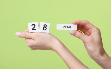 Block calendar with date april 28 in female hands on green background