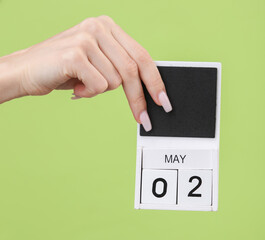 Block calendar with date may 02 in female hand on green background