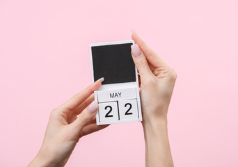 Block calendar with date may 22 in female hands on pink background