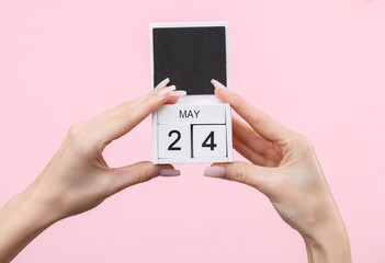 Block calendar with date may 24 in female hands on pink background