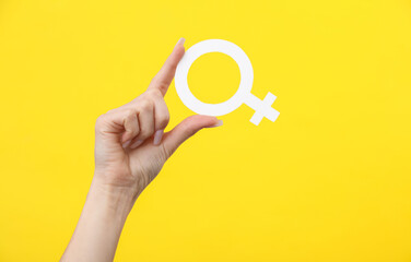 Woman's hand holding the female gender symbol of venus on a yellow background