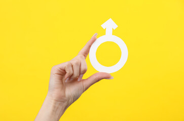 Female hand holding male gender symbol sign on yellow background