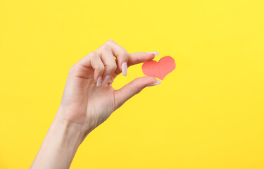 Fototapeta na wymiar Hand holding a paper-cut heart on a yellow background