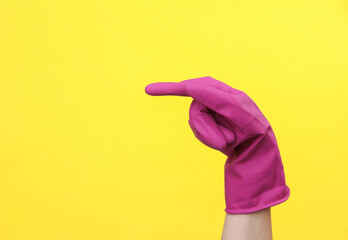 Hand in purple rubber cleaning glove points to the side on a yellow background. House cleaning and...