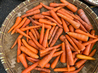 fresh, organic and imperfect carrots on round bamboo tray being sold at traditional market