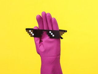 Hand in purple rubber cleaning glove with 8 bit pixel sunglasses on a yellow background. House...