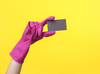 Hand in purple rubber cleaning glove holding business card on a yellow background. House cleaning and housekeeping concept