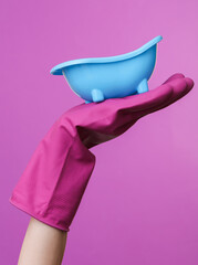 Hand in purple rubber cleaning glove holding toy bath on purple background.