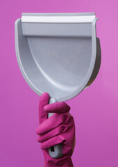 Hand in purple rubber cleaning glove holding scoop on purple background. House cleaning and housekeeping concept