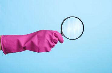 Hand in purple rubber cleaning glove holding magnifying glass on blue background. House cleaning...