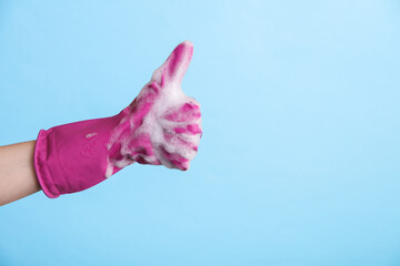 Hand in purple rubber cleaning glove and foam shows thumbs up on blue background. House cleaning and housekeeping concept