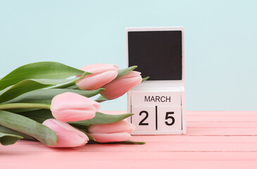 Block wooden calendar with the date March 25 and tulips on a pastel background. Spring composition