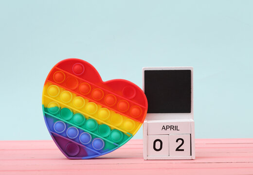 Calendar with date april 02 and pop it antistress heart shaped device on pastel background