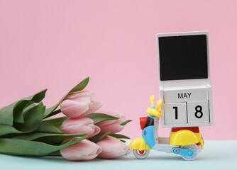 Block wooden calendar with the date may 18 on toy moped and tulips, pastel background