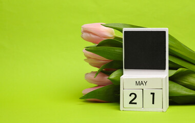Block wooden calendar with the date may 21 and tulips on a green background. Spring composition