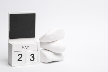 Block wooden calendar with the date may 23 and white pebbles stack on white background.