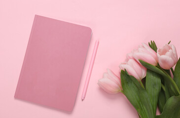 Bouquet of pink tulips with notebook on a pink background. Top view