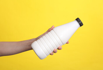 Female hand holding a bottle of yogurt on a yellow background