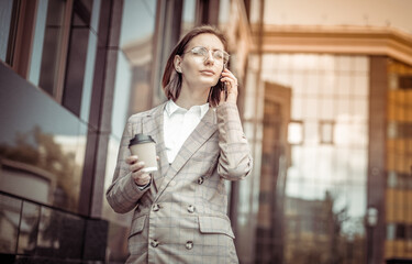 Young modern business lady talking on the phone and drinking coffee on the go.