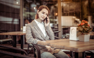 Young woman talking on phone while sitting at a table in an outdoor cafe