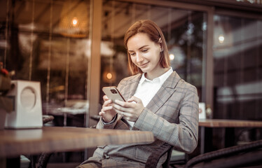 Young woman using phone while sitting at a table in an outdoor cafe