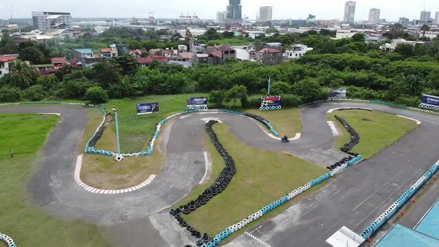 Drone shot of a Go Kart establishment but has a motorbike sampling the track. The drone is taking the shot from top to bottom. The Kart Track is in the city beside some residential houses.