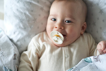 baby with pacifier in bed before sleep. Pretty six-month old baby boy. Realistic home portrait