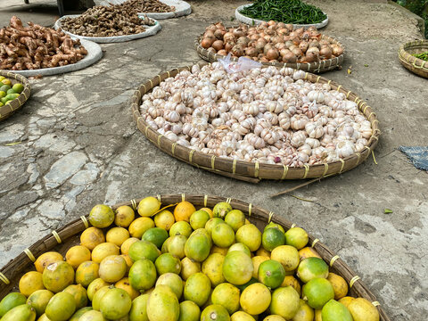 various vegetables tomatoes, chilli, red onion, corn, carrot, lime, garlic being sold at asian traditional market. colorful vegetables on round bamboo tray at traditional market floor
