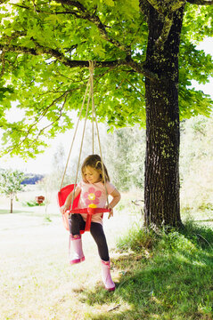 3 year old girl in rubber boots sitting in red swing in back yard, Sweden