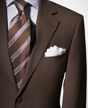 Detail of a bown suit jacket with shirt, white handkerchief and brown striped necktie