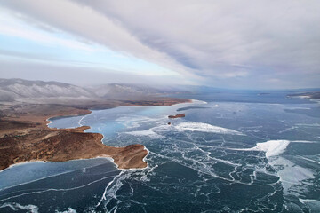 Frozen Lake Baikal in December from the air. Cloudy stormy sky, clear ice in the cracks. Winter landscape.