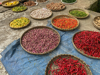 various vegetables tomatoes, chilli, red onion, corn, carrot, lime, garlic being sold at asian traditional market. colorful vegetables on round bamboo tray at traditional market floor