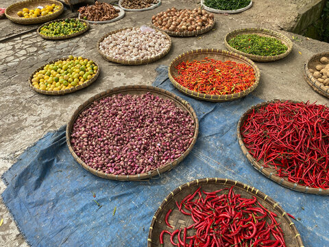 various vegetables tomatoes, chilli, red onion, corn, carrot, lime, garlic being sold at asian traditional market. colorful vegetables on round bamboo tray at traditional market floor