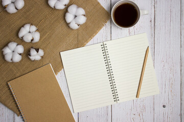 Notebook, cotton flowers and coffee over the white wooden table. 