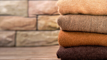 stack of cashmere sweaters in different shades of brown on a brick wall background, copy space, concept advertising banner