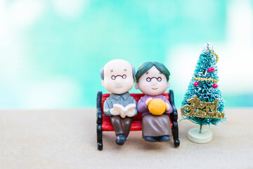 Obraz na płótnie Canvas Miniature elderly couple sitting on the bench with Christmas tree, elderly home care concept