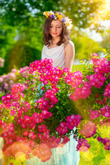 Naklejka premium Spring sexy fantasy woman enjoys standing near flowering pink roses. Outdoor portrait of young beautiful happy smiling lady posing. Youth, romantic and lifestyle concept. Copy, empty space for text