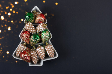 Christmas tree composition of tree decorations in the form of pine cones in red green and gold on black background with a place for text