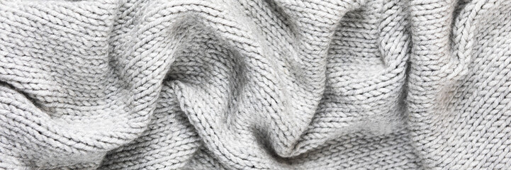 Knitted gray background. Close-up of a knitted blanket. Wavy folds material. Knitted warm grey sweater or scarf. Banner