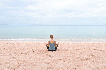 Fototapeta premium The girl is sitting in the lotus position and meditating on the sand on the beach