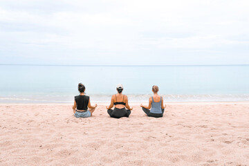 Fototapeta premium three girls are sitting in the lotus position and meditating on the sand on the beach