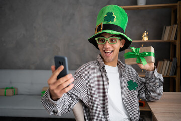 Happy man in leprechaun hat holding smartphone video calling talking to friend in virtual video...
