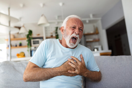 Senior man presses hand to chest has heart attack suffers from unbearable pain, Mature man with pain on heart in living room. Senior man suffering from bad pain in his chest heart attack at home