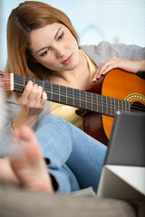 beautiful young woman playing guitar while sitting on sofa
