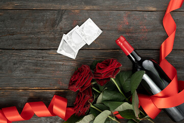 Valentine's day or date, bottle of wine, red roses and condoms on wooden background. February 14...