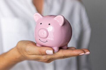 female hands puts a coin in a pink piggy bank. The concept of saving money or savings, investment