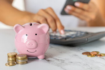 Close-up of a woman's hands counting expenses on a calculator with a piggy bank on an office desk....