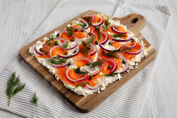 Homemade Cream Cheese Lox Bagel Board with Salmon on a white wooden background, side view.
